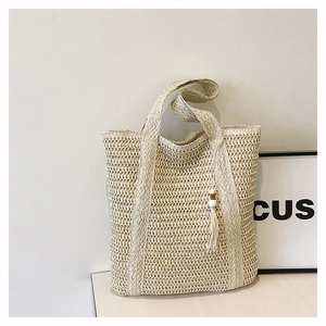 Close-up of beige woven straw tote bag featuring tassel charm and intricate crochet detail