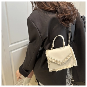 Detail view of cream-white mini square bag with fringe trim and golden chain strap