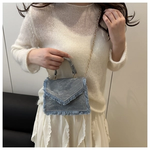 Detail of blue denim mini crossbody bag with raw fringe edges and gold chain strap