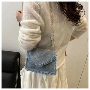 Detail showing the light blue denim square bag with fringe trim and gold chain strap