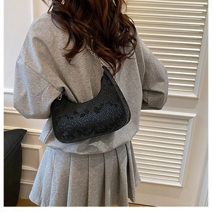 Chic black snake-texture hobo bag with gold chain strap worn by a model in a minimalist room