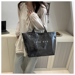 Glossy black tote bag with white TOTE BAG print worn by model in minimalist office scene