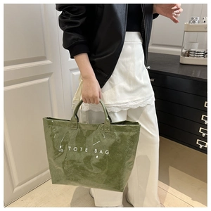 Detail der grünen, glänzenden Faltenstruktur und weißer TOTE BAG-Aufdruck auf PVC-Handtasche