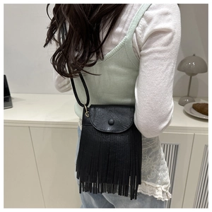Close-up of black leather crossbody bag featuring stylish tassels and a round decorative buckle