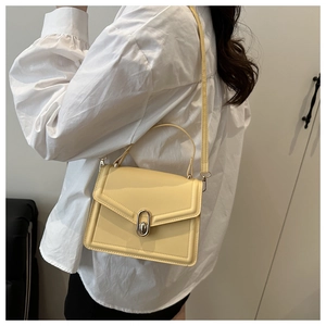 Detail of pale yellow square crossbody bag with silver clasp and top handle on shoulder