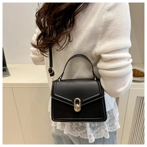 Model wearing a black crossbody bag with gold twist lock in a modern indoor setting