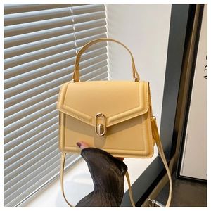 Detailopname van een gele handtas met een gouden ovale metalen draaisluiting op de flap