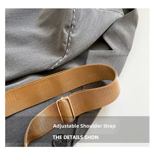 Detail of adjustable tan woven shoulder strap with gold metal buckle on a grey bag