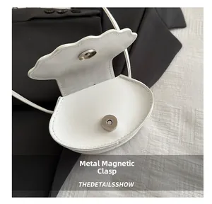 Macro detail of the magnetic hardware buckle on a white shell-shaped crossbody bag