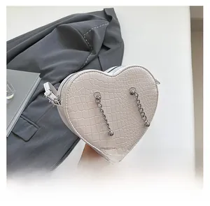 Detailed view of white heart-shaped crossbody bag with crocodile pattern and silver chains