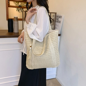 Minimalist beige woven tote bag with wooden bead tassel shown in a cafe setting
