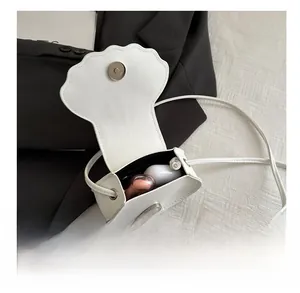 Close-up of white shell-shaped leather crossbody bag showing storage for wireless earbuds