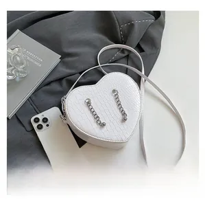 Detail of white heart-shaped crossbody bag with crocodile texture and metal chains