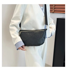 Detail of black woven half-moon crossbody bag with golden zipper on white blazer