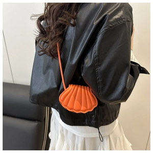 Chic orange shell crossbody bag with glossy texture worn over a black leather jacket