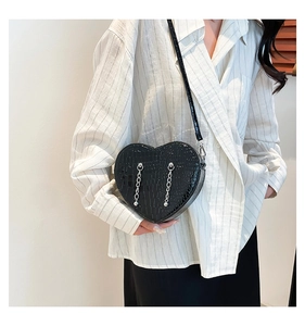 Close-up of black heart-shaped crossbody bag with crocodile texture and silver chains