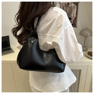 Detailed view of black glossy moon-shaped hobo bag worn on shoulder for commute style