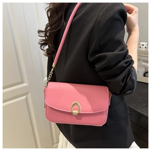 Pink PU leather crossbody bag with golden horseshoe clasp worn over a black blazer