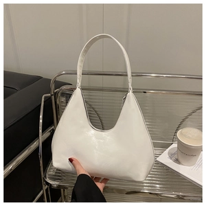 Glossy white hobo shoulder bag held in a modern minimalist lifestyle setting