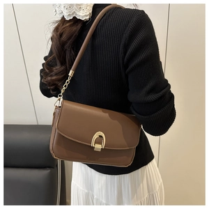 Brown leather shoulder bag with gold horseshoe clasp shown worn on model's shoulder