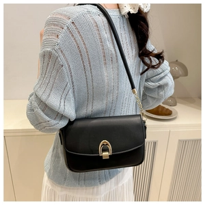 Model wearing a black leather shoulder bag with a gold arch lock and chain strap