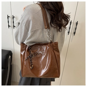 Detail of brown leather tote bag with silver bow and tennis racket charm accessory