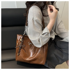 Detail of a brown leather tote bag with silver bow accent and novelty keychain charms