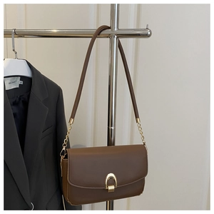 Détail d'un sac à main en cuir marron foncé avec boucle fer à cheval dorée et chaîne