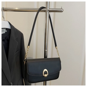 Détail du sac à rabat en cuir noir avec boucle fer à cheval dorée et chaîne