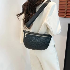 Sac bandoulière noir tissé avec fermetures dorées porté par un mannequin en blanc