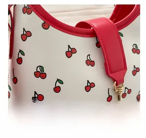 Detail of white leather shoulder bag featuring red cherry prints and golden hardware