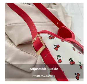 Detail of adjustable red leather strap with gold metal buckle on cherry pattern bag