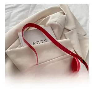 Detail showing red leather handle and golden metal buckle on cherry print tote bag