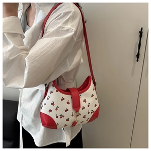 Detail of a white cherry print shoulder bag featuring red edges and gold hardware