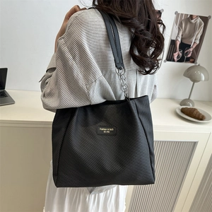 Black striped tote bag with chain shoulder strap shown worn by a model in modern room
