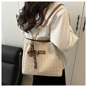 Detail of woven straw tote bag featuring leather trim, chain strap, and striped bow