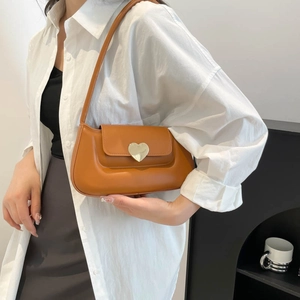 Borsa sottobraccio in pelle marrone con grande fibbia a cuore dorata indossata da modella