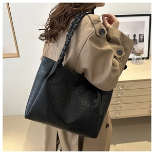 Dettaglio di grande borsa tote nera con tracolla a trama spessa indossata da modella