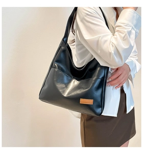 Detail of minimalist black PU leather tote bag with a brown patch on a model