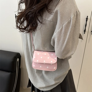 Pink polka dot mini crossbody bag with a glossy finish and long shoulder strap