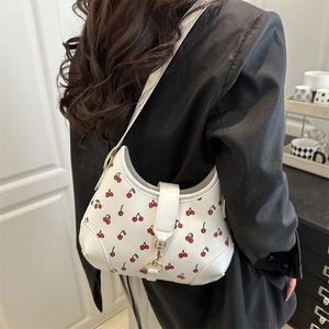 White crescent shoulder bag with red cherry print and gold hardware worn with black suit