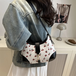 Retro shoulder bag with cherry print, black leather trim and gold buckle on a model
