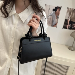 Minimalist black tote bag with knot handles and gold lettering shown in hand