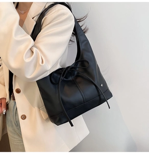 Detail of black tote bag with bow accent and heart-shaped metal stud on model