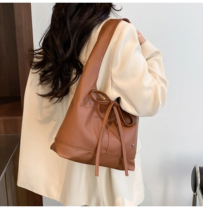 Detail of a brown leather shoulder bag featuring a decorative long tassel bow tie design