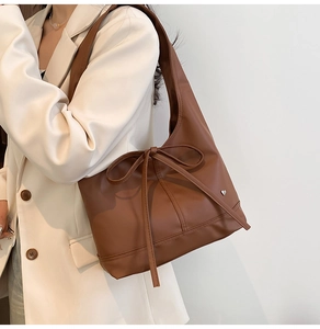 Detail of a brown shoulder bag with a bow tie and silver heart charm on beige blazer
