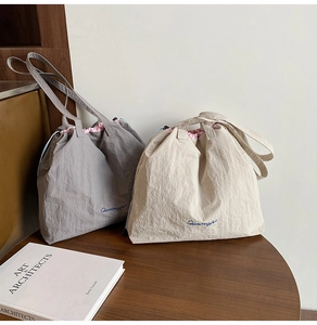 Détail de sacs fourre-tout en nylon gris et beige avec cordon et broderie bleue