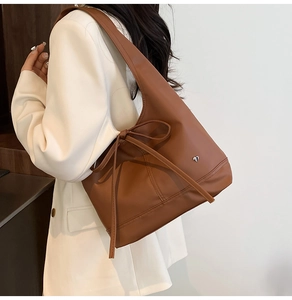 Close-up of brown tote bag with ribbon bow and silver heart logo on white blazer
