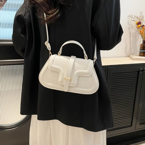 Chic white leather shoulder bag with gold buckle and curved piping detail on a model