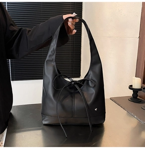 Close-up of black leather tote bag with large bow and silver heart pendant